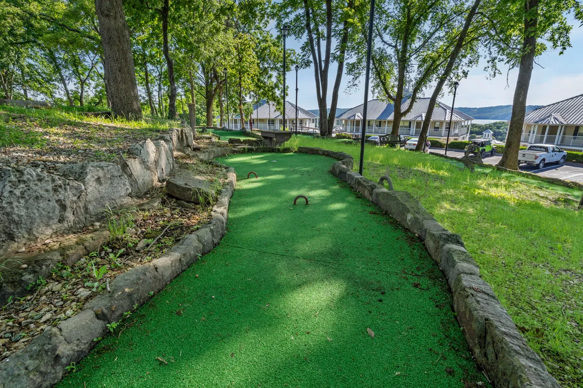 A playful mini-golf course winds through lush greenery and natural rock formations, inviting friendly competition and group fun. Benches and picnic areas are visible, offering space for gathering and socializing in nature.