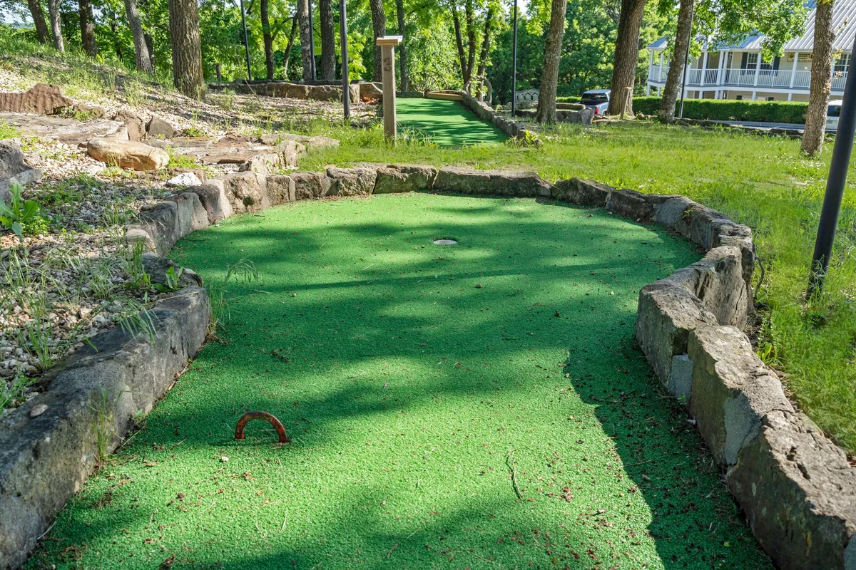 A cheerful mini-golf course is set amid green synthetic turf, natural stone borders, and tall trees. The playful arrangements and inviting environment capture family-friendly fun and outdoor leisure.