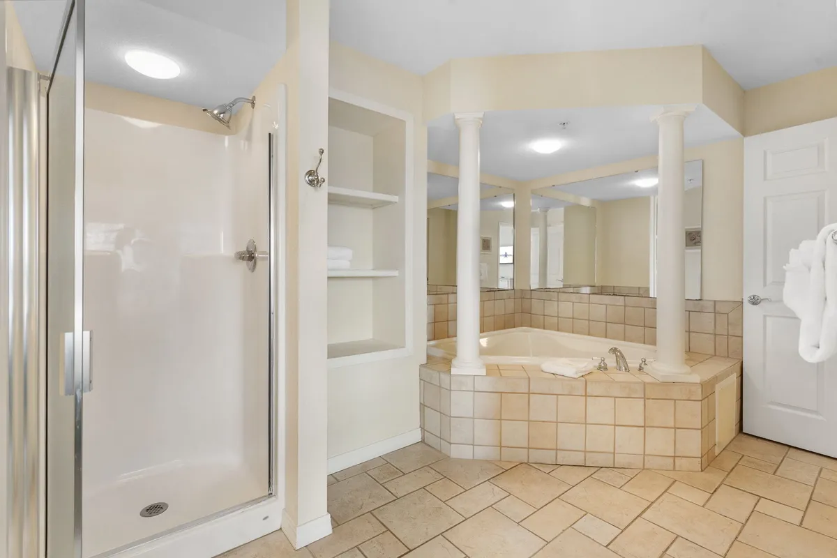 This interior image showcases a spacious bathroom with a large jacuzzi tub, a separate shower stall, elegant columns, and shelves, all bathed in soft, calming lighting. The setting exudes an atmosphere of luxury and relaxation, perfectly aligning with the ensuite offering a soaker tub and walk-in shower.