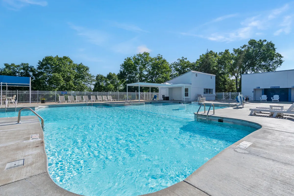 A sparkling outdoor swimming pool is framed by lounge chairs and shaded cabana areas, surrounded by mature trees for a tranquil yet social setting. The pool is inviting for both play and relaxation after a day at the lake.