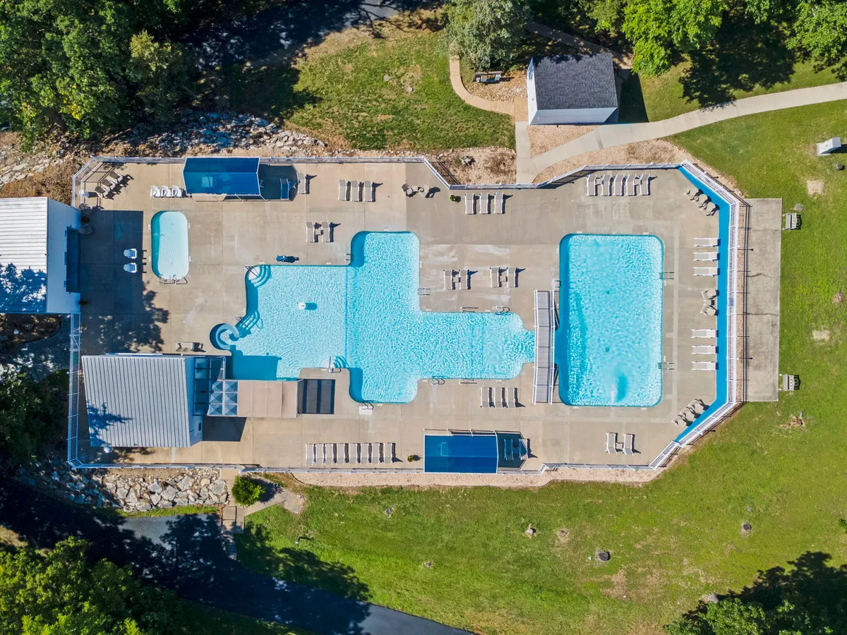 A vibrant outdoor swimming pool area surrounded by lush greenery and well-placed lounge chairs. The space is bustling with activity, including children playing games and guests relaxing poolside, all set against a backdrop of natural beauty.