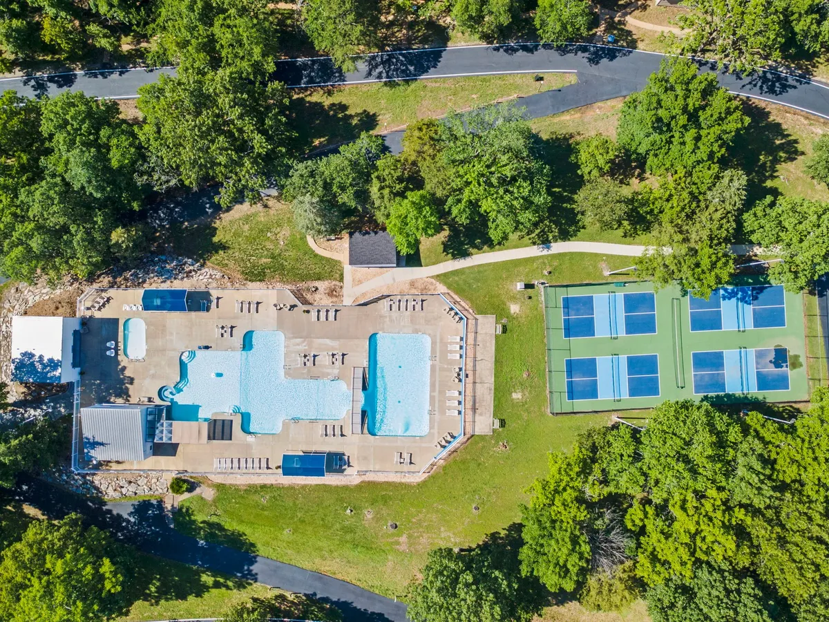 This image captures a sunny exterior view of the resort's swimming pools, tennis courts, loungers, and lush surrounding greenery. The communal areas are bustling with possible activities and relaxation, embodying the essence of resort life.