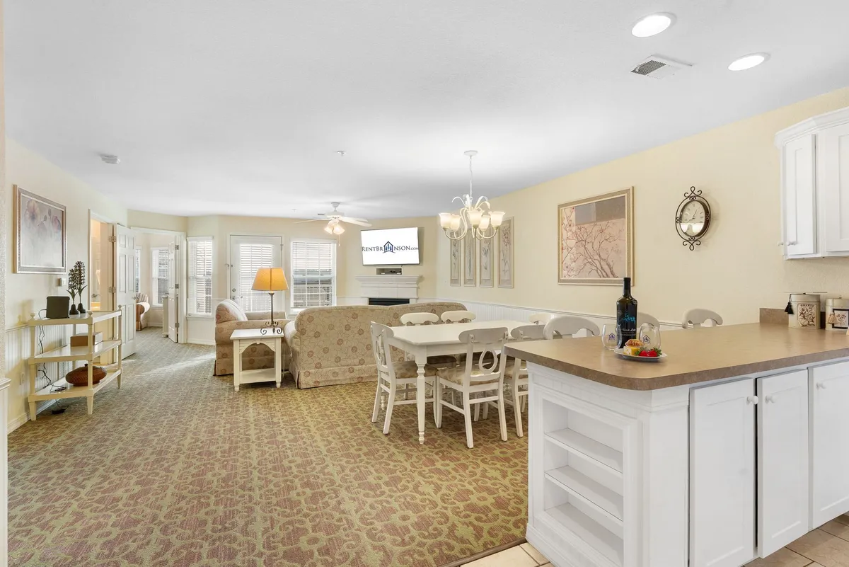 This image captures an inviting and cozy living and dining area, highlighting a spacious open layout with a dining table, comfortable sofa, kitchen counter, stylish chandelier, and wall art. The scene suggests ample room for both people and pets to relax, socialize, and enjoy time together.