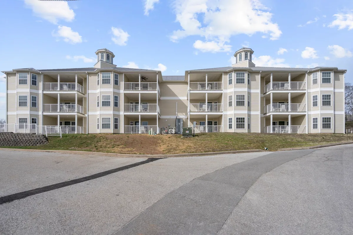 The resort's exterior architectural design with wrap-around balconies, a lush green lawn, and hints of community gatherings. The scene suggests relaxation on the balconies, social events, and enjoying changing seasonal views from the comfort of your accommodation.