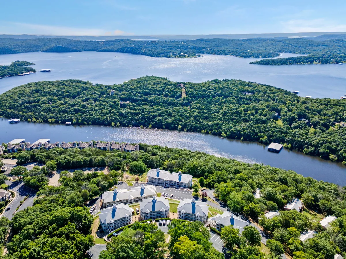 A wide, inviting view of the expansive Table Rock Lake framed by surrounding hills, with a cluster of resort buildings in the foreground. The calming scene features hints of water activities like boating and gentle trails along the lakeshore, all bathed in golden sunset light.