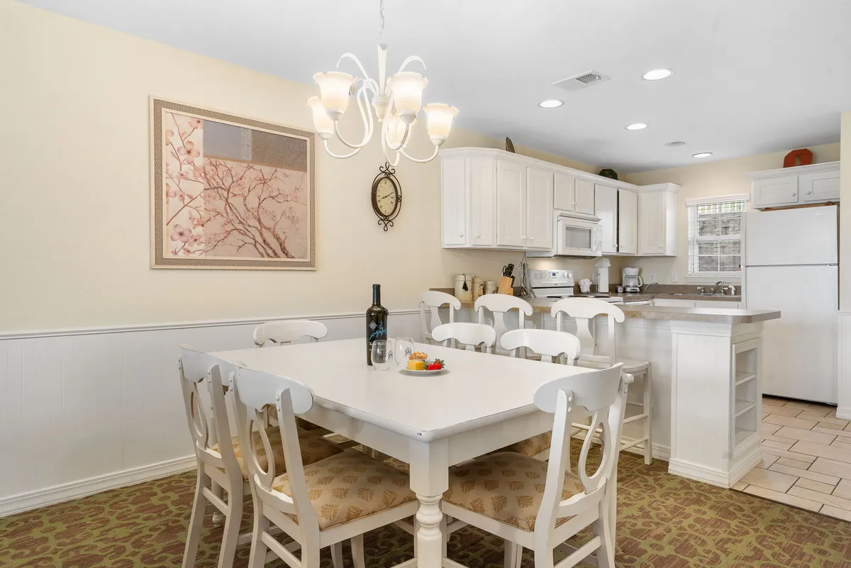 A view of the dining area with a large dining table under a stylish chandelier, seamlessly connected to a modern kitchen counter. The setup invites family meals, celebrations, and easy entertaining, reflecting a welcoming atmosphere.