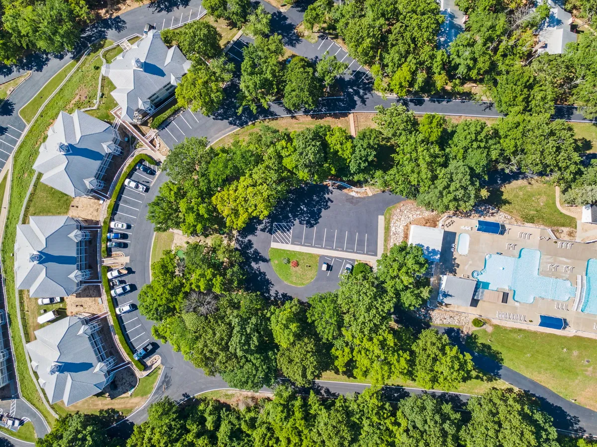 A welcoming swimming pool surrounded by lush greenery, with resort buildings in the background and plenty of open space for guests to relax and socialize. The scene conveys a sense of relaxation, togetherness, and inviting outdoor fun, ideal for the summer months.