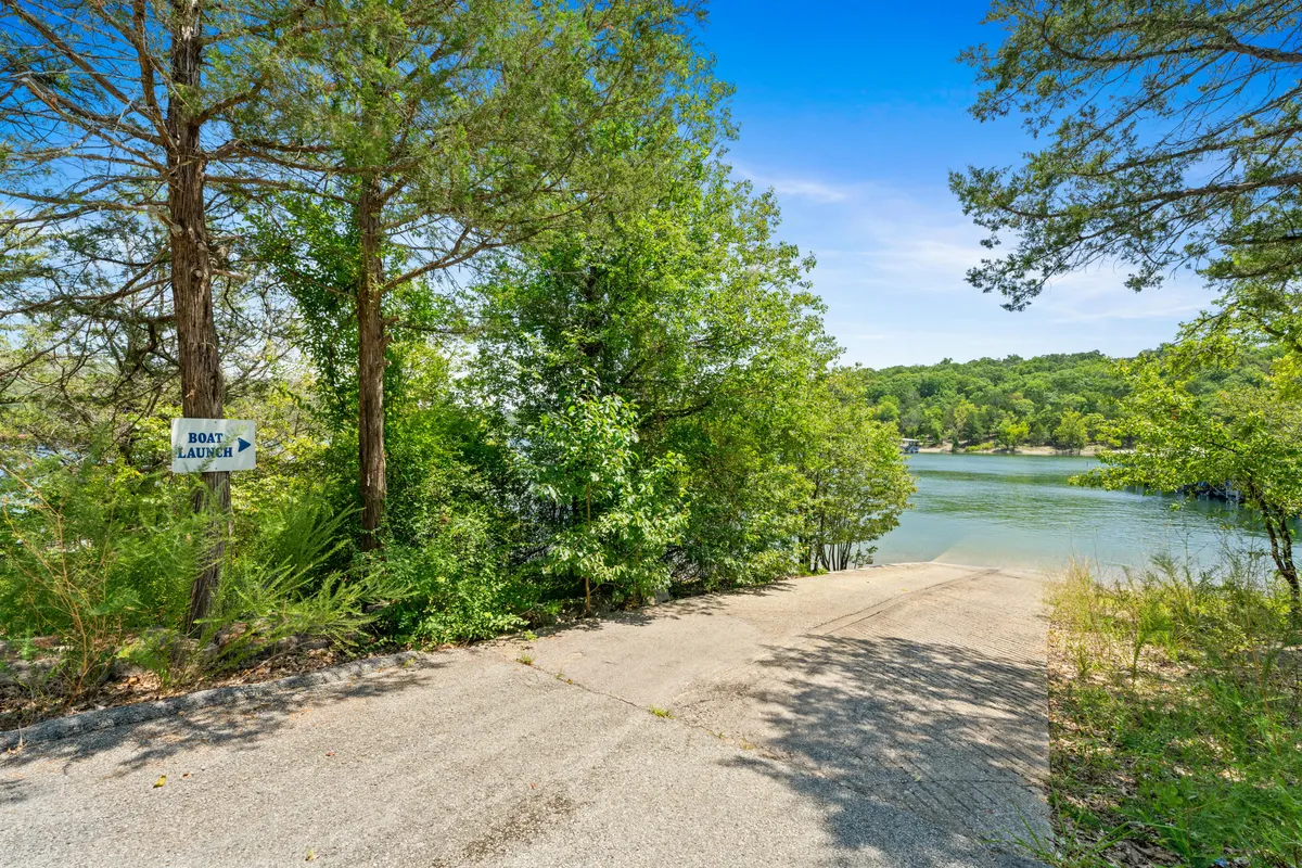 A waterfront scene showcases a concrete boat ramp, a clear view of the lake, tree-lined shores, and a sign marking the boat launch area. The setting feels peaceful and ready for lakeside adventure.